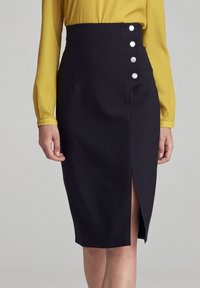 Czarna ołówkowa spódnica z wysokim stanem, z rozporkiem do uda i pięcioma metalowymi guzikami po boku. Gładka tekstura tkaniny.