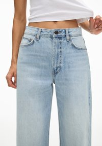 Light blue denim wide-leg jeans with a high waist, featuring five pockets, button closure, and faded texture. Visible stitching accents.
