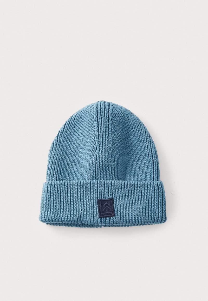 Gebreide beanie in zacht blauw met een opgerolde omslag. Heeft een donkerblauw logo-etiket en een verticale ribstructuur door het hele ontwerp.