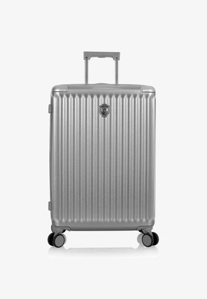 Valise rigide argentée avec des rainures verticales, quatre roues, poignée rétractable et emblème central sur le panneau avant.