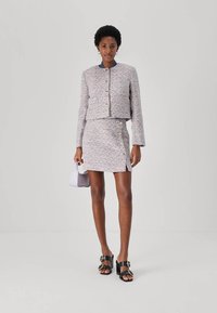 Veste et jupe en tweed multicolore texturé avec des boutons dorés. Associées à un sac à main violet clair et à des sandales à talons noirs.