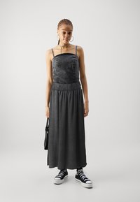 Robe maxi en denim gris avec un corsage ajusté, une taille smockée et une jupe fluide, associée à des baskets montantes noires.