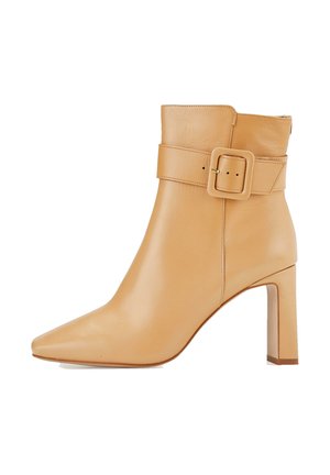 Bottine en cuir fauve avec un bout carré, une large bride avec boucle, et un talon bloc. Texture lisse et design minimaliste.