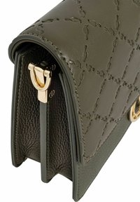 Zielona skórzana torebka o zarysowanym kształcie, z wytłoczonym wzorem i złotymi akcentami na zapięciu. Teksturowane wykończenie po bokach.