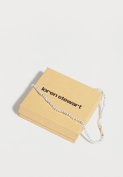 Κολιέ με πέρλες και χρυσό κούμπωμα, τοποθετημένο πάνω σε μπεζ κουτί με την ετικέτα "loren stewart" πάνω σε λευκό φόντο.