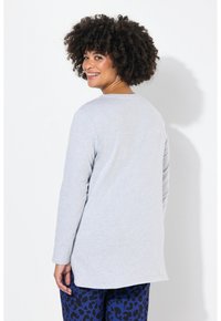 Lichtgrijze lange mouw shirt met een afgeronde zoom en een zachte textuur, gecombineerd met blauwe broek met een zwart luipaardpatroon.