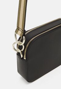 Borsa a tracolla in pelle nera con hardware dorato, chiusura con doppia zip e una tracolla texturizzata con dettaglio "ESTABLISHED".