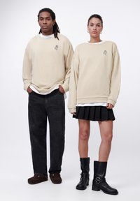 Beige oversized sweatshirts with embroidered design, dark jeans, black pleated skirt, and knee-high boots. Smooth fabric texture, casual style.