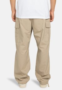 Pantaloni cargo beige con polsini aderenti, dotati di tasche laterali e una vestibilità comoda. Realizzati in un tessuto leggero e resistente per il massimo comfort.