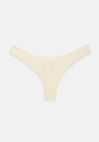 Kremowe majtki typu string z prążkowanej tkaniny z falbanką z koronki na krawędziach, ułożone płasko na jednolitym tle.
