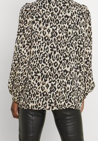 Leopardmönstrad blus i kräm och svart, med puffiga ärmar och avslappnad passform, matchad med svarta läderbyxor.