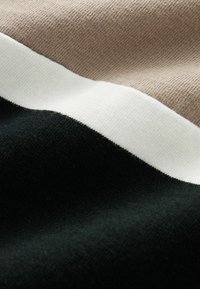 Tissu tricoté en noir, beige et blanc, avec des rayures horizontales distinctes. La texture semble lisse et douce.