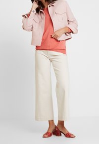 Jasnoróżowa krótka kurtka z dwoma przednimi kieszeniami, w połączeniu z koralowym swetrem i szerokimi beżowymi spodniami. Obuwie to czerwone, wzorzyste klapki.