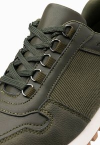 Zielone trampki wykonane z połączenia gładkiej skóry i teksturowanej tkaniny, z sznurowaniem, metalowymi przelotkami i kontrastową podeszwą.