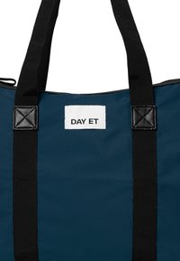 Borsa a sacca blu navy con manici neri, caratterizzata da un'etichetta bianca con la scritta "DAY ET". Il tessuto sembra resistente e leggero.