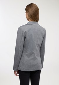 Blazer grigio in tessuto lavorato, caratterizzato da un colletto con revers, maniche lunghe e una linea aderente. La vista posteriore mostra linee pulite e una sartoria curata.