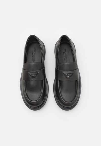 Fekete bőr loafers cipők párnázott talppal, tetején egy sávval és egy háromszög alakú logóval díszítve. Simaszerkezet és lekerekített forma.