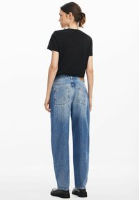 Svart kortärmad t-shirt i kombination med ljusblå högmidjade jeans med rak benpassform och subtila blekningar. Svarta skor synliga.