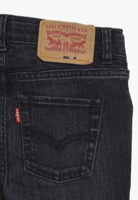 Jeans de mezclilla oscura con una etiqueta de cuero que presenta gráficos en rojo y negro, diseño del bolsillo trasero y un pequeño logo de Levi's en rojo en la costura lateral.