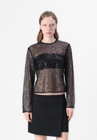 Schwarzes, glitzerndes Langarm-Oberteil mit transparentem Oberteil und schwarzem, solidem Zentrum. Kombiniert mit einem figurnahen schwarzen Rock. Minimalistisches Design.