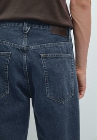 Jeans blu scuro con un design classico, in materiale denim, due tasche posteriori e un'etichetta in pelle sulla cintura.