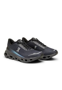 Zapatillas deportivas negras con parte superior de malla texturizada, que presentan un acento en degradado azul, suela acolchada con secciones recortadas y cordones negros.