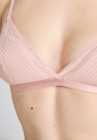 Bralette rosa claro com um design texturizado em formato de nervuras, apresentando uma renda ao longo do decote e uma faixa inferior lisa e elástica.