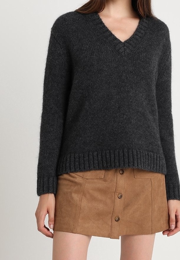 Femme portant un pull tricoté à col en V gris foncé associé à une mini-jupe en daim camel avec boutons sur le devant.