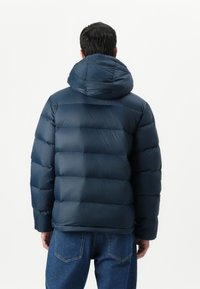 Navy blue puffer jacket with a hood, featuring quilted sections and a smooth, shiny texture. The design includes a relaxed fit.