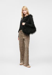 Melnas mākslīgās kažokādas soma ar teksturētu virsmu, nēsāta uz pleca, apvienota ar leopardu raksta platām biksēm un melnu garām piedurknēm.