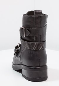 Botín negro de cuero hasta el tobillo con un acabado texturizado, detalle de hebilla y correa con tachuelas, un tacón bajo y un diseño de punta redonda.