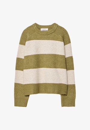 Frau trägt einen grün-weißen gestreiften Pullover, hellblaue Jeans, Sneakers mit Kuhmuster und hält eine braune Umhängetasche am Riemen.