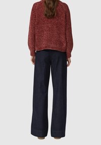 Roter, strukturiert gestrickter Pullover mit ballonförmigen Ärmeln, kombiniert mit locker sitzenden dunkelblauen Jeanshosen mit weitem Bein und umgeschlagenem Saum.