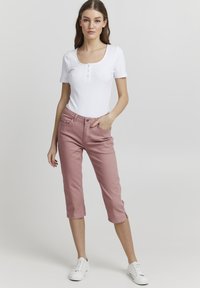Top corto blanco ajustado de manga corta con detalle de botones, combinado con pantalones cropped rosas. La modelo lleva zapatillas blancas. Diseño simple, textura suave.