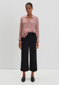 Overhemd met knopen in rood en wit gestreept, gecombineerd met hoge zwarte broek met een losse pasvorm en wijde pijpen.