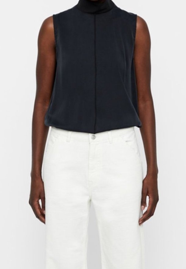 Blouse sans manches bleu marine foncé avec un col montant, texture lisse et détail de couture centrale, associée à un jean blanc à jambes larges.