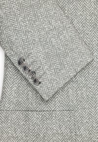 Tkanina marynarki w szarym wzórze w jodełkę z teksturowanym wykończeniem. Posiada cztery ciemne guziki na mankietach i kieszeń.
