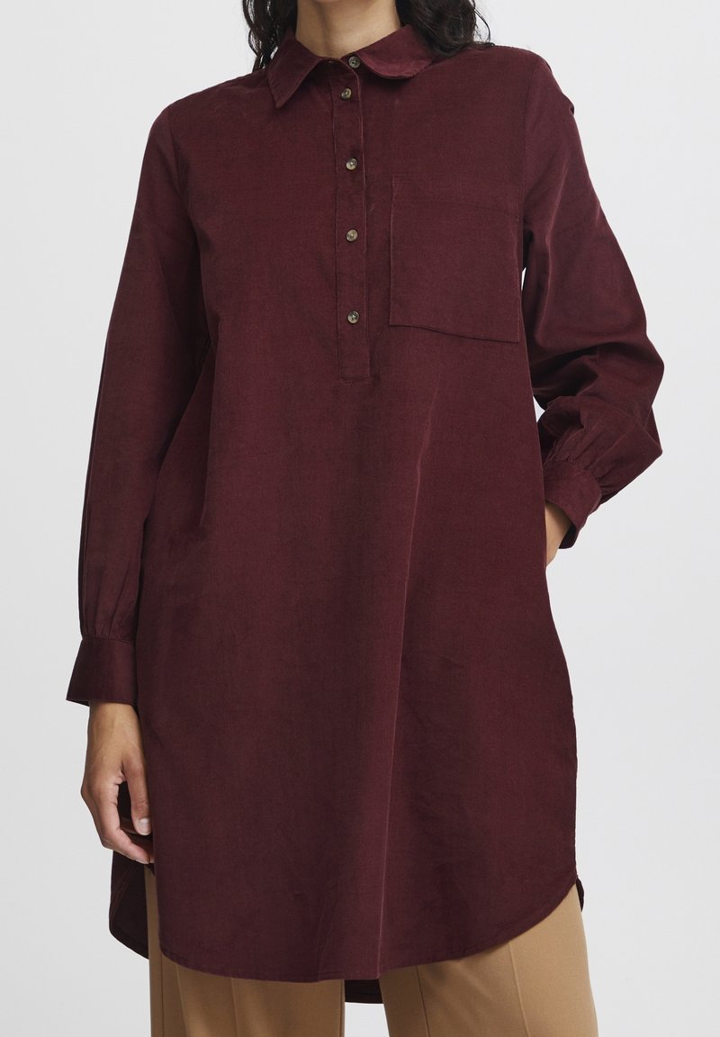 Chemise à manches longues bordeaux avec col, devant boutonné et poche poitrine unique. Texture douce et coupe décontractée avec poignets froncés.