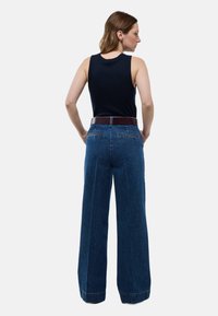 Pantalons en denim à jambes larges de couleur bleu foncé, avec une taille haute, des coutures discrètes et une ceinture en cuir. Les poches arrière sont visibles.
