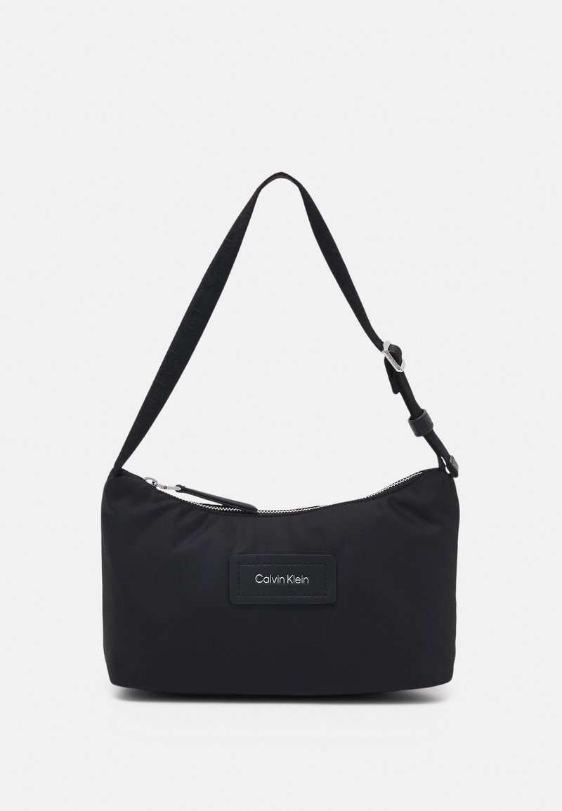 Musta nailoninen olkalaukku vetoketjulla, suorakaiteen muotoinen, säädettävä hihna ja Calvin Klein -logopatchi edessä.