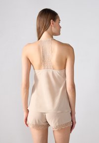 Tan satin pyjamassæt med en detaljeret ryg af blonder, slanke stropper og blondekanter på shortsen, der fremhæver en glat tekstur.