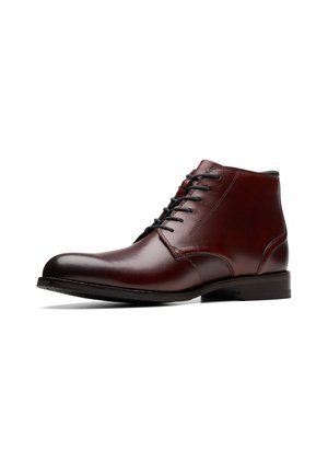 Bottine en cuir marron poli avec des lacets noirs et un petit talon, montrée de profil sur fond blanc.