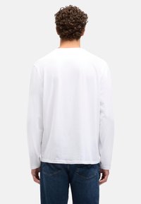 Hvid langærmet skjorte med rund halsudskæring, glat tekstur og løs pasform, kombineret med blå denimjeans med baglommer.