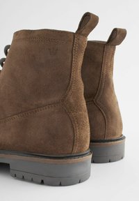 Brune ruskindsankelstøvler med en solid sort gummisål, med en tekstureret overflade og minimalistiske designdetaljer på hælen.