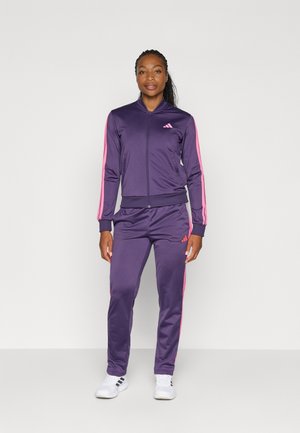 Chándal deportivo morado con rayas rosas, hecho de una tela suave. La chaqueta con cremallera y los pantalones a juego tienen puños ajustados y un logo de Adidas.