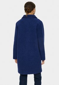 Marinblå, texturerad kappa med krage och långa ärmar, med en lös passform som når till mitten av låret. Ryggvy visas.