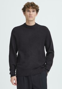 Pulover cu decolteu rotund, de culoare gri �închis, din țesătură tricotată netedă. Are mâneci lungi și detalii cu dungi la guler și tiv. Design simplu.