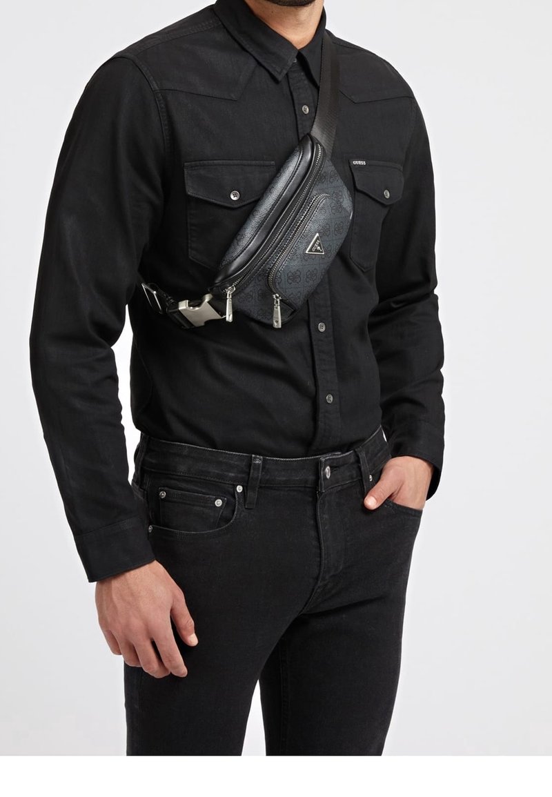 Borsa a tracolla in tessuto nero con scomparti con zip, superficie testurizzata e logo triangolare, indossata a tracolla da una persona in camicia nera a pulsante.