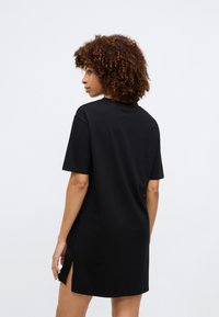 Μαύρο oversized φόρεμα t-shirt με κοντά μανίκια, πλαϊνές σχισμές και στρογγυλή λαιμόκοψη, φτιαγμένο από μαλακό βαμβακερό υλικό.