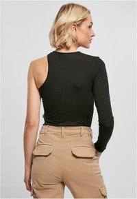 Svart langermet skjorte med asymmetrisk design. Den ene ermen dekker hele armen; den andre siden er ermeløs. Brukt med beige cargo-bukser.
